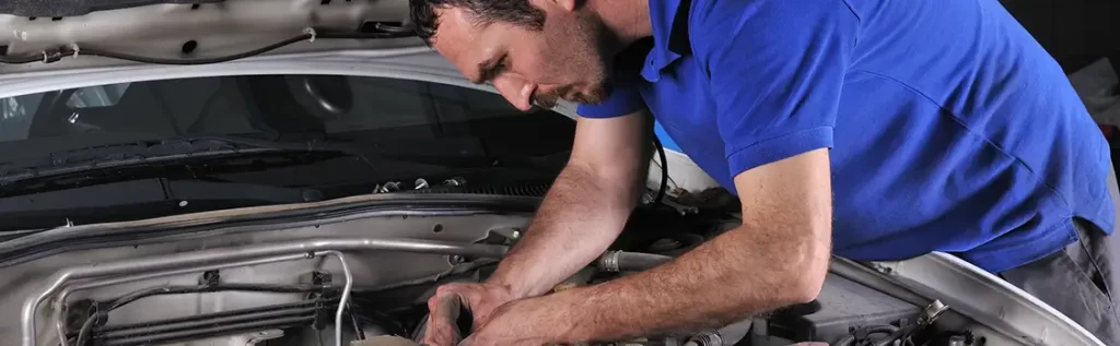 man in blue shirt working under hood of a car