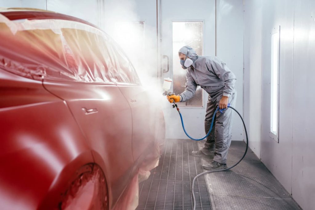 technician at an auto paint shop painting a car red